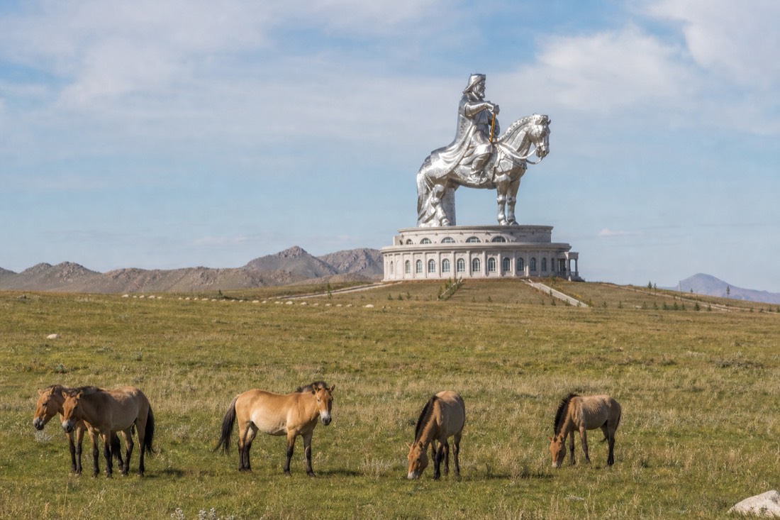 The giant stainless steel Chinggis Khaan equestrian statue rising above open grassland at Tsonjin Boldog, a common stop on Gorkhi-Terelj day trips from Ulaanbaatar, low hills in the background under a clear sky